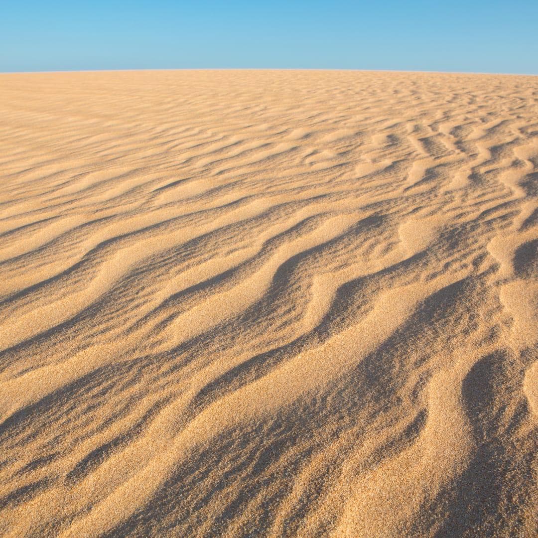 Waves of golden sand stretch under a clear blue sky.