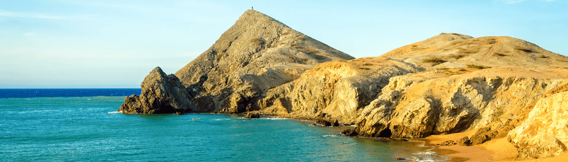 A scenic coastal view featuring rocky cliffs and turquoise waters under a clear sky.