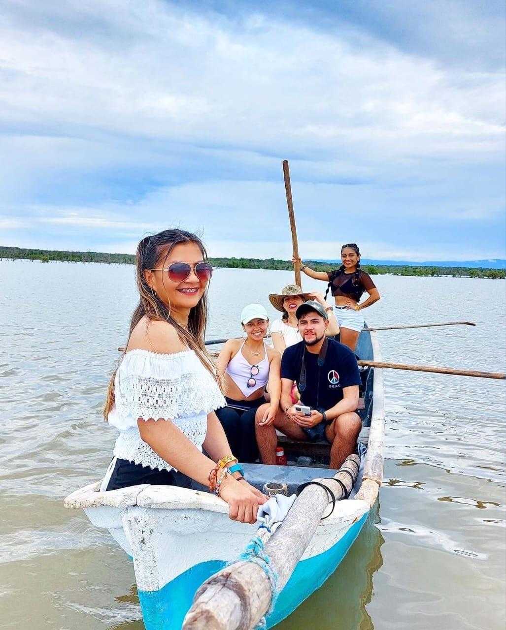 A group of five people poses for a photo in a small boat on calm water under a cloudy sky.