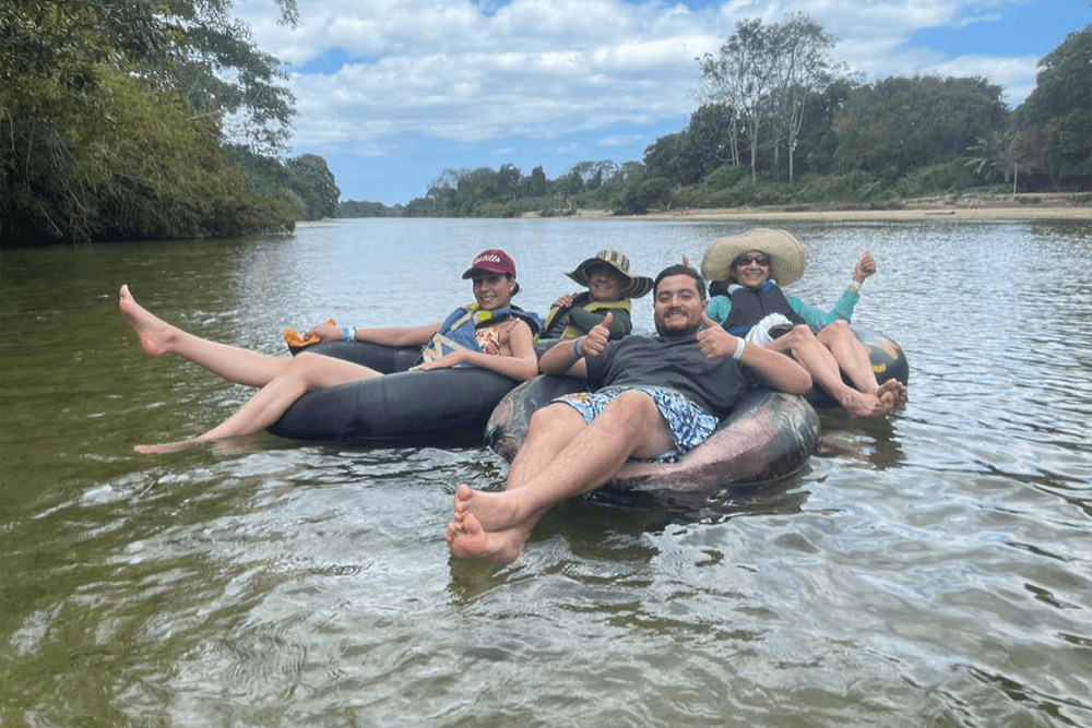 Five people relax on inner tubes in a river, enjoying the sunny day.