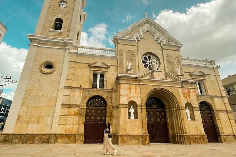 A woman walks past a historic stone church under a cloudy sky.