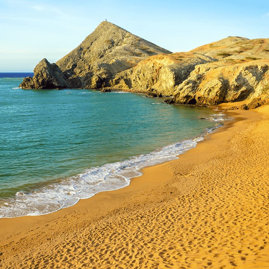 A serene beach with golden sand, gentle waves, and rocky cliffs under a clear sky.