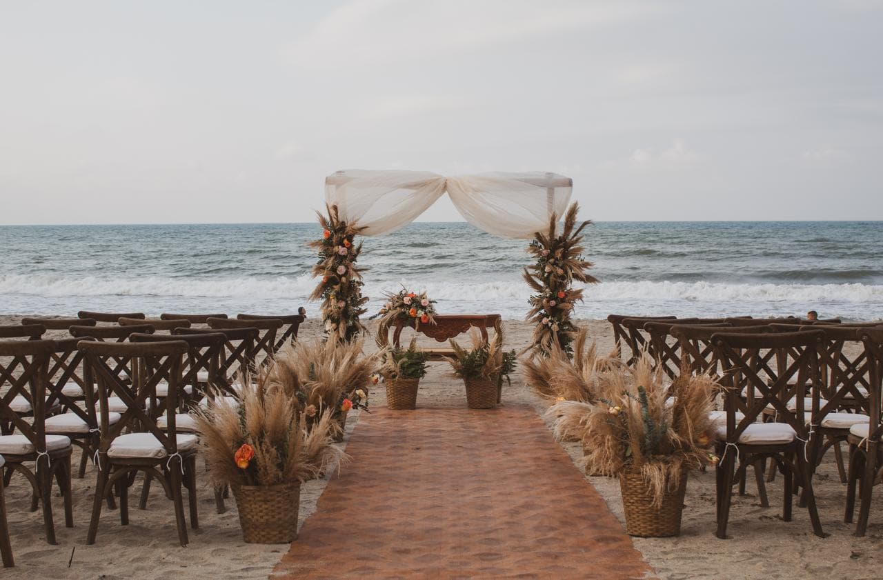 A beautifully decorated beach wedding setup with chairs, floral arrangements, and an arch by the ocean.