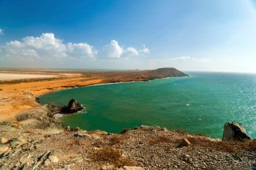 Scenic view of a turquoise sea meeting a rugged coastline under a blue sky with clouds.